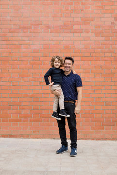 Portrait of smiling father carrying son at brick wall