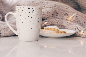 Cozy knitwear and a cup of coffee with a cake on white marble windowsill against white window background. Copy space.