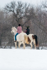 two girls riding horses bareback in winter on a snow covered field