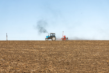 Fototapeta premium Blue tractor with a red seeder works on the field on a bright sunny autumn day