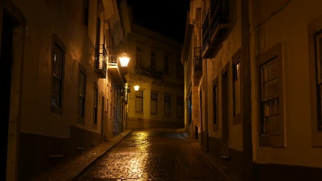 Old town of Faro, Algarve, Portugal at night. Cobblestones street, lit by yellow street lamps. Pan up.