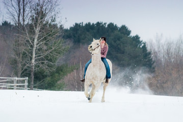 blonde young woman riding her horse through snow bareback on a winter day