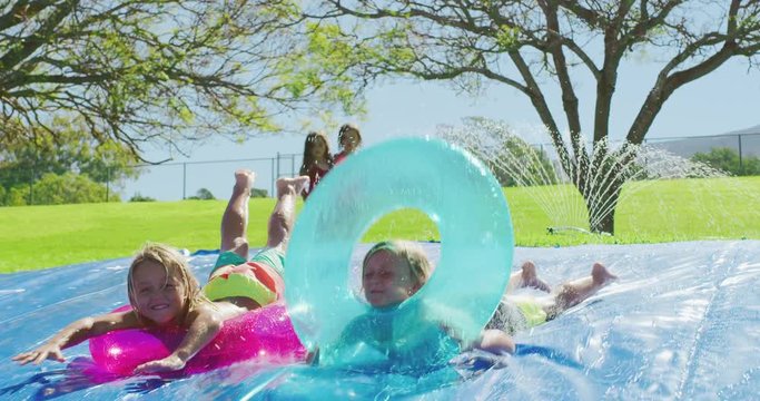 Kids summer water slide fun, two smiling boys sliding down waterslide