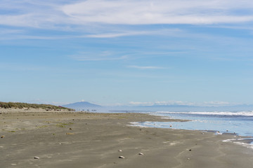 Beautiful empty beach during sunny day with mountains on the horizon, costal line with blue sky