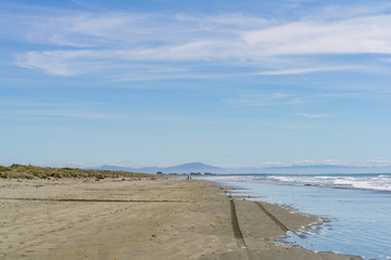 Wast empty beach during sunny day with mountain peaks in the background and with tire marks in the foreground
