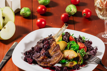 Roasted ribs in blackbarry sauce with vegetables, brussels sprout, cherry tomatoes and apple on wooden background