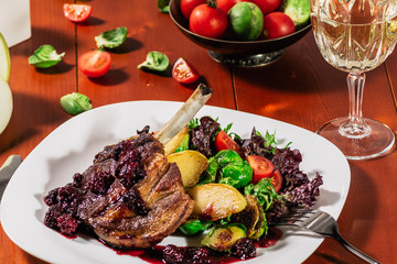 Roasted ribs in blackbarry sauce with vegetables, brussels sprout, cherry tomatoes and apple on wooden background