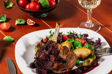 Roasted ribs in blackbarry sauce with vegetables, brussels sprout, cherry tomatoes and apple on wooden background