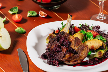 Roasted ribs in blackbarry sauce with vegetables, brussels sprout, cherry tomatoes and apple on wooden background