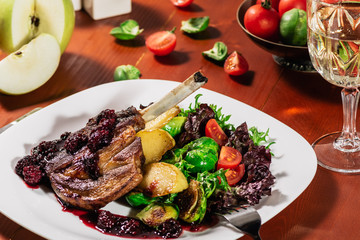 Roasted ribs in blackbarry sauce with vegetables, brussels sprout, cherry tomatoes and apple on wooden background