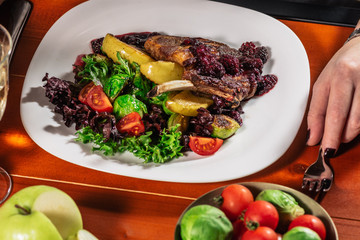 Roasted meat with brussel sprouts, cherry tomatoes, salad leaves and apple for garnish. girls hand with white wine