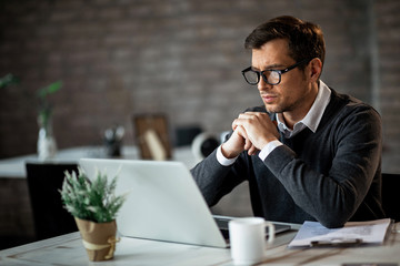 Serious businessman reading something on laptop while working in the office.