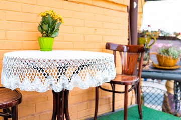 Empty table outside restaurant cafe with chairs on street and yellow flowers in flowerpot potted plant setting with nobody in summer