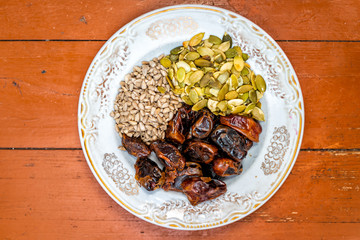 Flat top closeup on wooden table of raw vegan healthy snack or ingredients with sunflower and pumpkin seeds, and dried dates for making truffles on table white plate