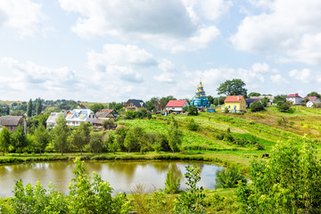 Obraz premium Landscape of farm green town and houses in summer in Rivne oblast village in Ukraine countryside during day with pond lake and church