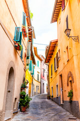Chiusi, Italy street alley in small historic medieval town village in Umbria vertical view during sunny day with orange yellow bright vibrant colorful walls