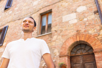 Fototapeta na wymiar Chiusi, Italy tourist man smiling on street alley with historic architecture in bokeh background wall in small historic medieval town village in Tuscany during sunny summer day