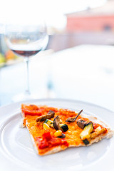 Closeup of pizza slice on white plate on balcony terrace by red wine glass bokeh background outside in Italy with vertical view in Tuscany