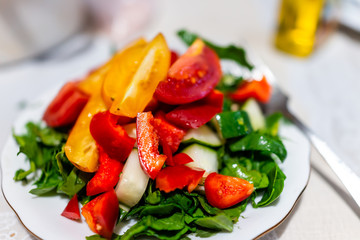 Closeup of fresh raw chopped vegetable salad with arugula greens and red and orange bell peppers, tomatoes, cucumbers on table for colorful vibrant healthy lunch meal