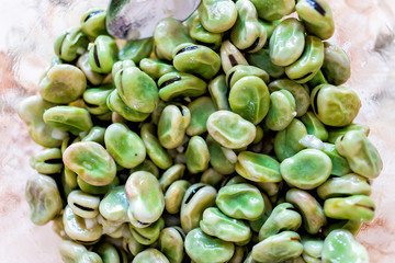 Macro flat top closeup view down of green fava broad beans in glass bowl for marinated in skin shell