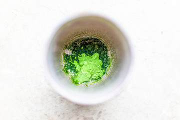 Flat top closeup of cup bowl with Japanese vibrant green tea color matcha powder on bottom with lumps and wet preparation macro showing detail and texture