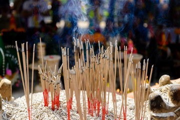 Many burning joss sticks and incense for worship Buddhism and Asian cultural belief which stand on fully ash censer with background of blurry smog and people in Temple. 