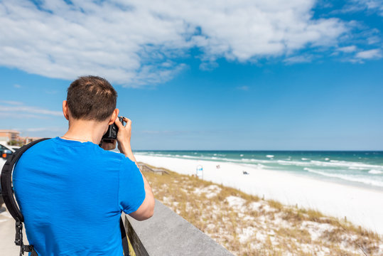 Destin Miramar beach city town village in Florida panhandle gulf of mexico ocean with photographer young man closeup in blue shirt taking picture photo of sand dunes with camera