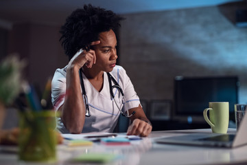 Pensive African American healthcare worker sitting at desk in doctor's office.