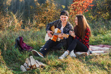 Young man playing on the guitar for his lovely girlfriend. Happy couple with guitar resting on picnic in spring park.