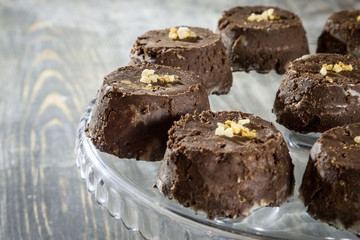 Individual small baked chocolate and walnut pudding cake, brown in color, on display on a glass plate put on a rustic wooden table