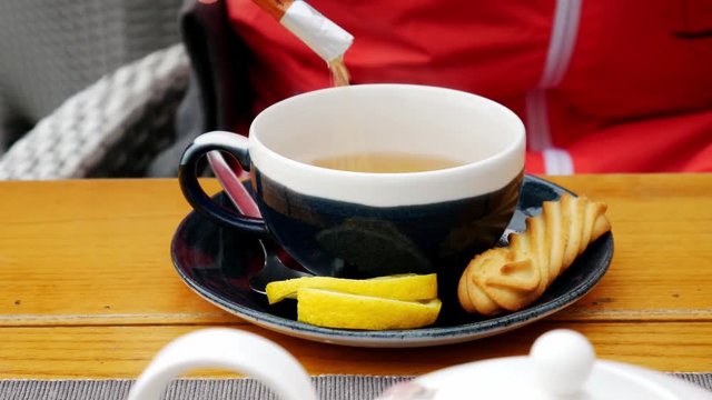 People and drinks concept - Woman hands pouring sugar to the cup of tea in cafe