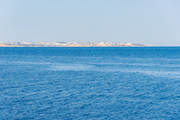 hotels and houses in the distance stand over a cliff above the blue sea