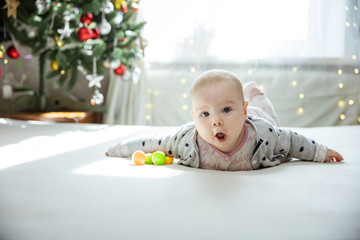 Surprised baby girl lying down on bed at home. Christmas tree in background.