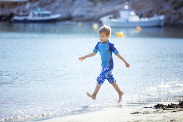 Happy young boy running along water edge  and making splashes