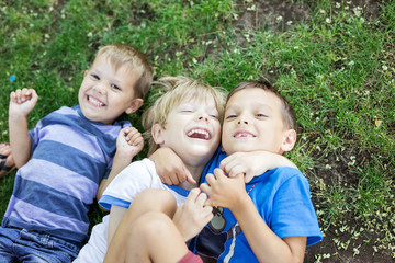Three happy young boys lying down on grass in summer park