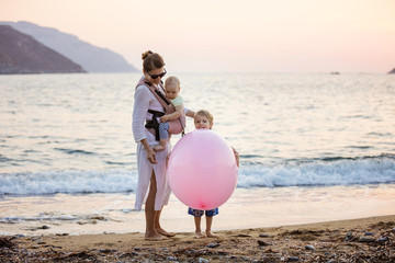 Young Caucasian woman with baby daughter iand son playing with huge pink balloon on beach