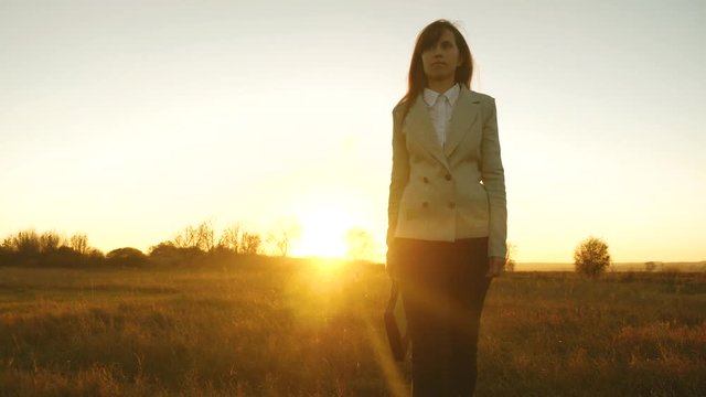 concept of successful business woman. woman in business suit with black briefcase in her hand is walking across field in rays of sunset. sexy business woman smiling.