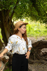 Women white skin lovely brown hair wearing a basketry hat brown red lip wear white shirt wearing black pants women standing poses photography portrait under the tree In the garden.