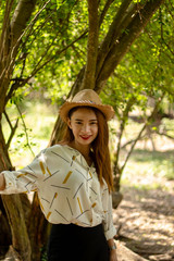 Women white skin lovely brown hair wearing a basketry hat brown red lip wear white shirt wearing black pants women standing poses photography portrait under the tree In the garden.