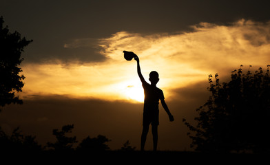 boy waving his hat to the setting sun. silhouette of a child at sunset
