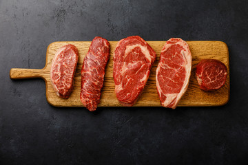 Variety of Raw Black Angus Prime meat steaks Top Blade, Denver, Rib Eye, Striploin, Tenderloin fillet Mignon on wooden board on dark background