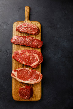 Variety of Raw Black Angus Prime meat steaks Top Blade, Denver, Rib Eye, Striploin, Tenderloin fillet Mignon on wooden board on dark background