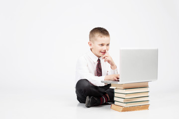 Little funny student Boy looking at tablet pc, seating  with school books and laptop computer on White background isolated