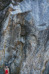 Woman wearing horn mask standing near big rock on sea shore