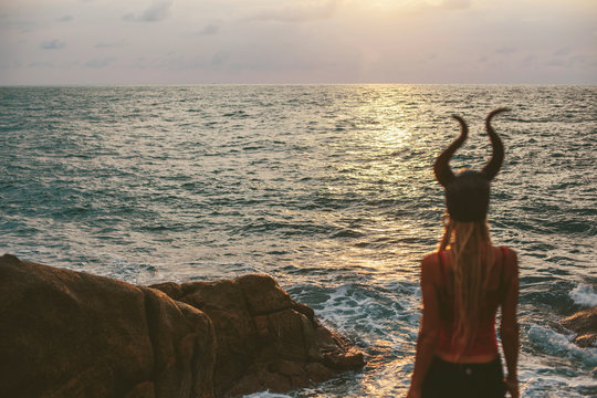 Woman wearing horn mask standing on cliff sea shore and enjoy sunset