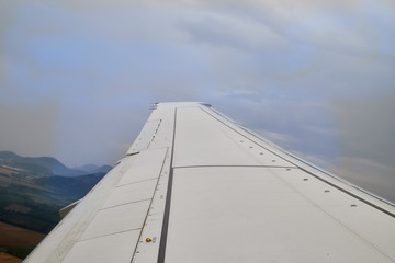 Fototapeta na wymiar View of airplane wing over clouds and mountains during take off or landing in airport