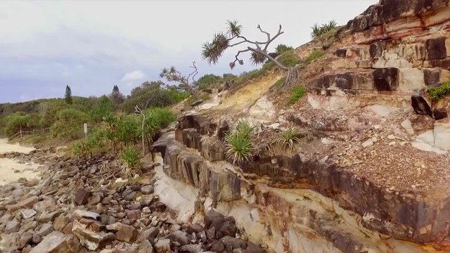 Aerial drone rising shot up a rocky cliff with spiky trees to reveal Mt Coolum