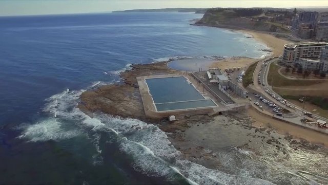 Aerial drone shot, late afternoon, flying south along the coast over the ocean baths and Merewether baths