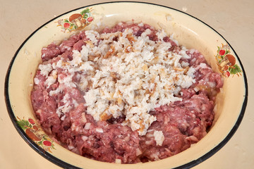 fresh beef and pork minced meat sprinkled with white onions and chicken egg and salt and pepper and white bread for making cutlets and schnitzel in a yellow iron plate. meat