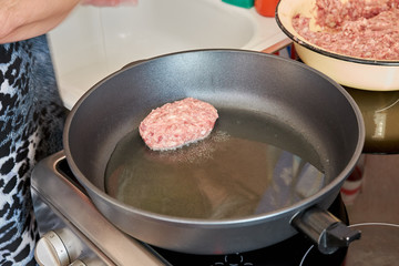woman at home in the kitchen fries meatballs made from pork and beef on a hot frying pan on an electric stove